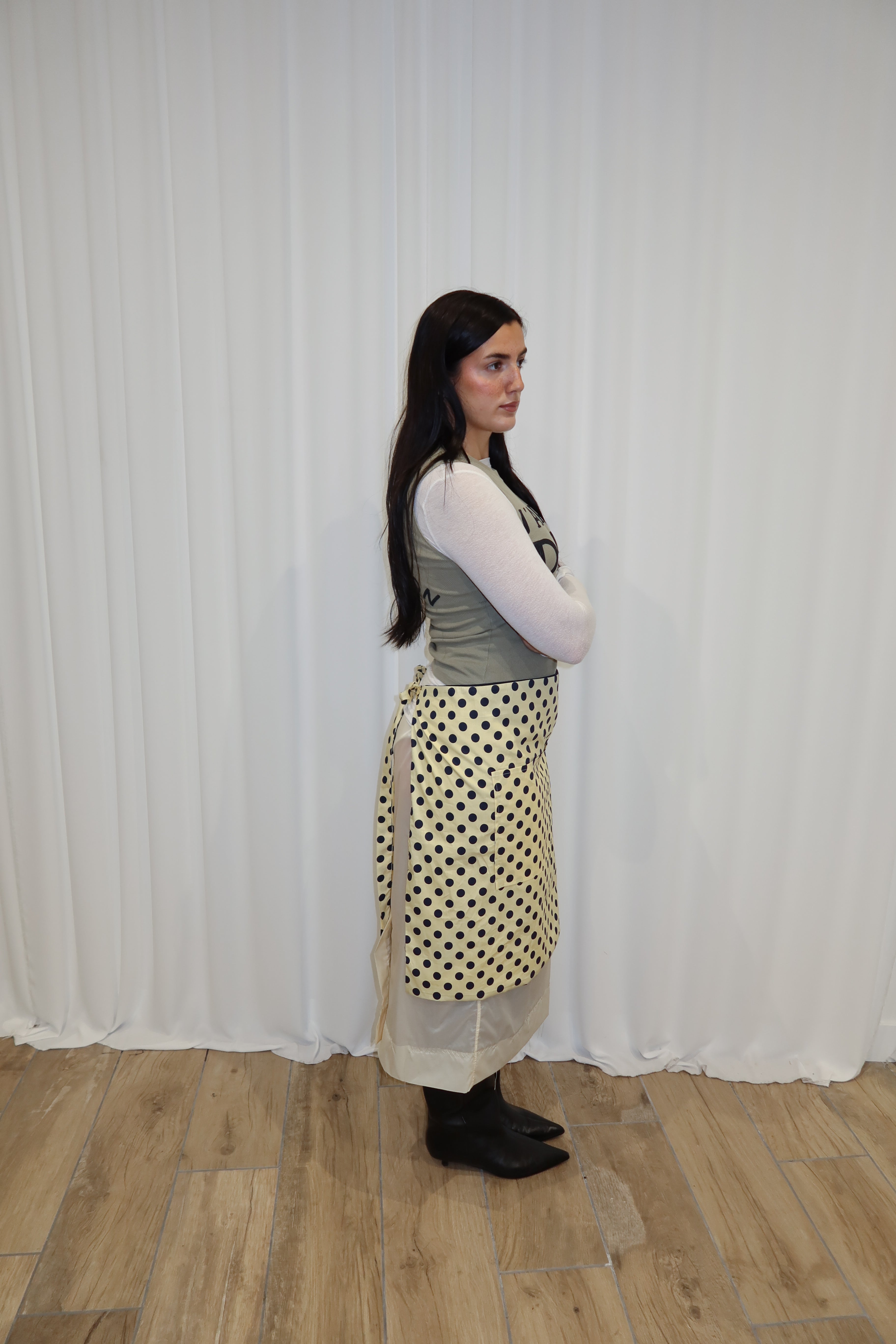 Woman wearing a polka dot apron standing against a white curtain.