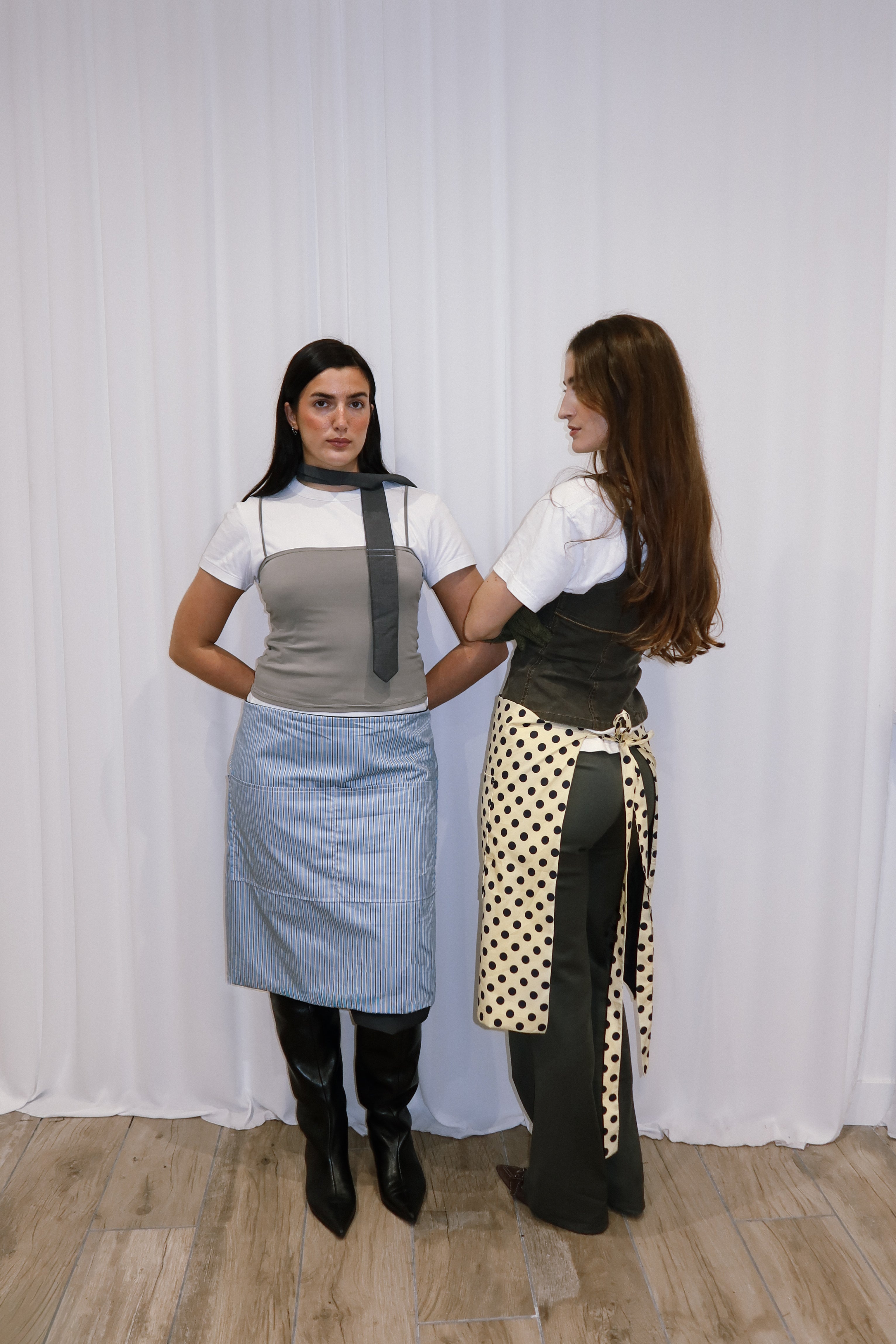 Two women wearing aprons standing against a white curtain.