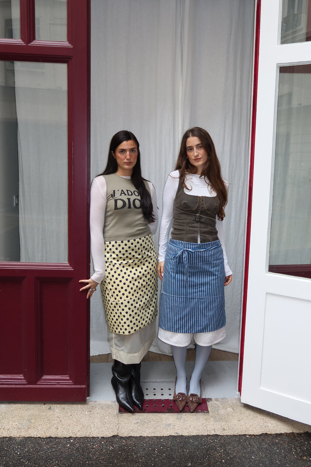 Two women standing in front of a door wearing aprons.