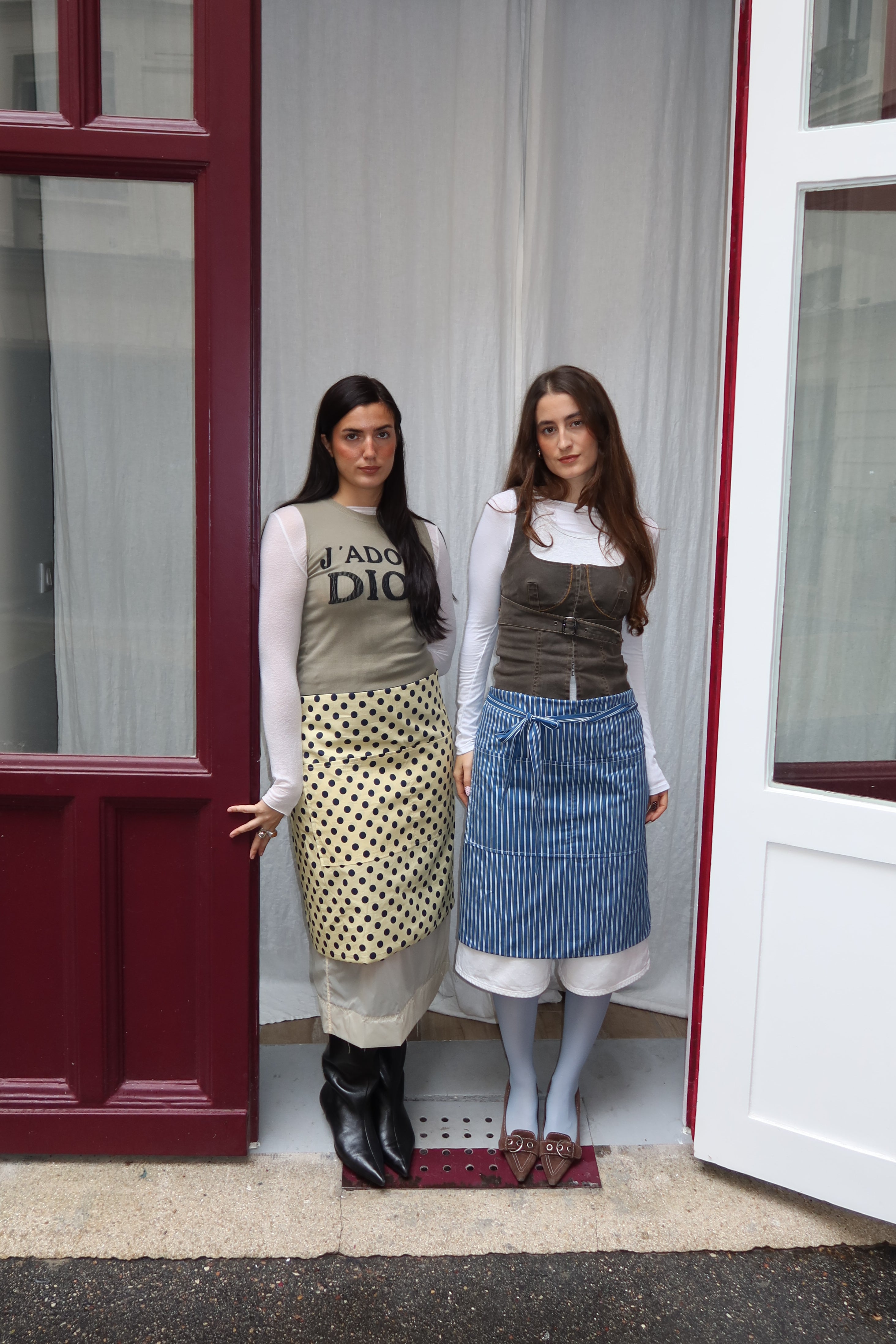 Two women standing in front of a door wearing aprons.