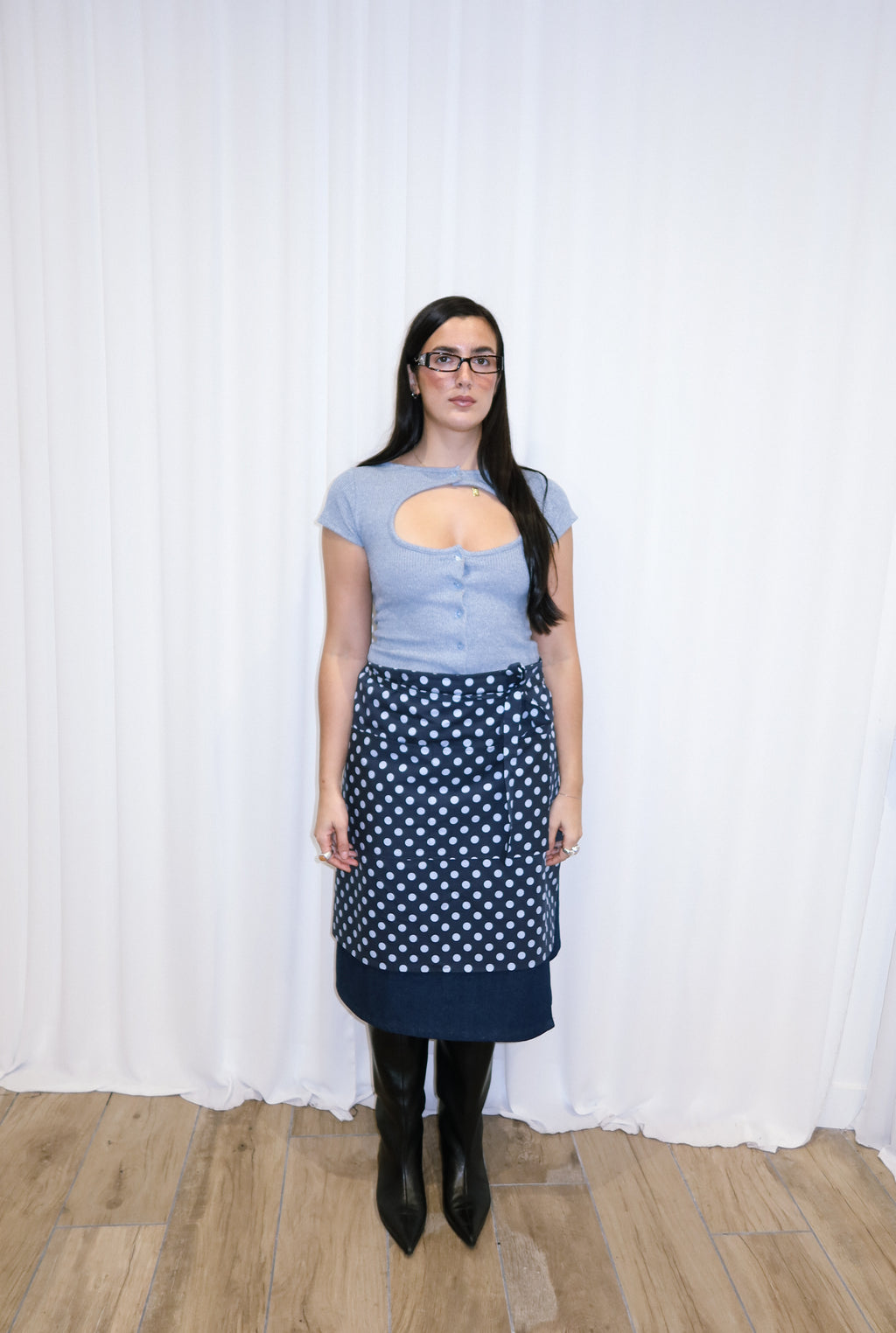 Woman wearing a navy polka dot apron against a white curtain background.