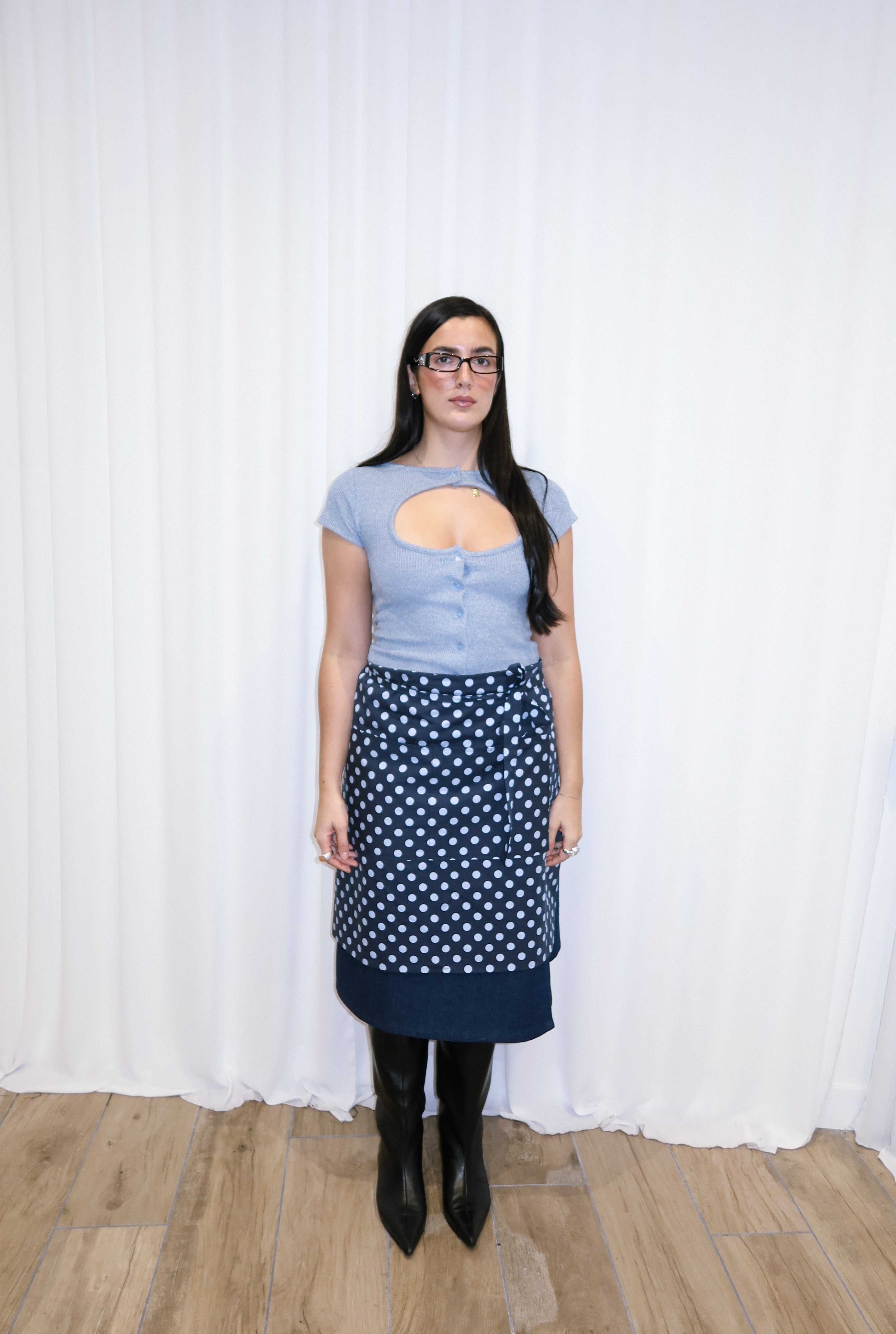 Woman wearing a navy polka dot apron against a white curtain background.
