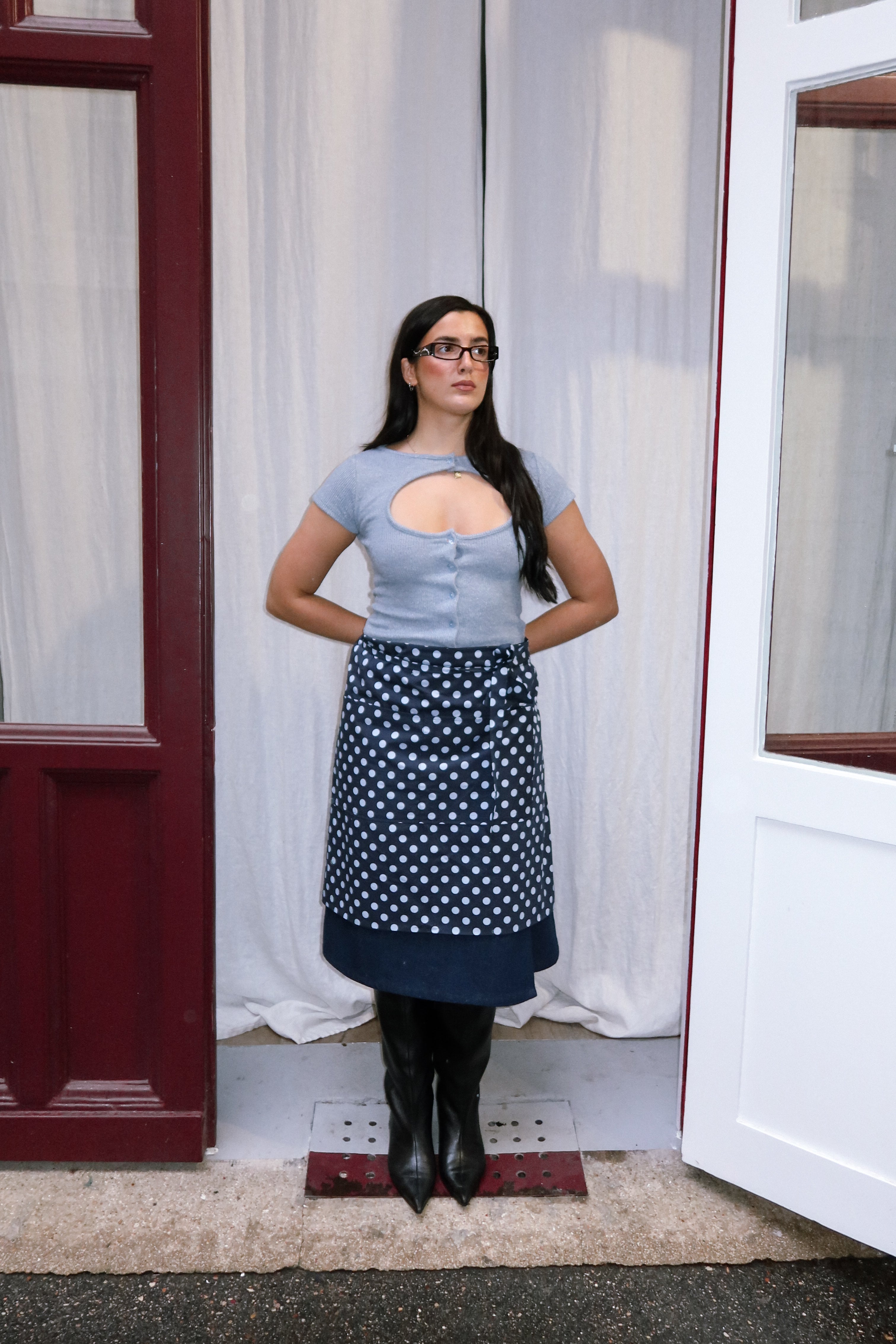 Woman wearing a navy polka dot apron against a white curtain background.