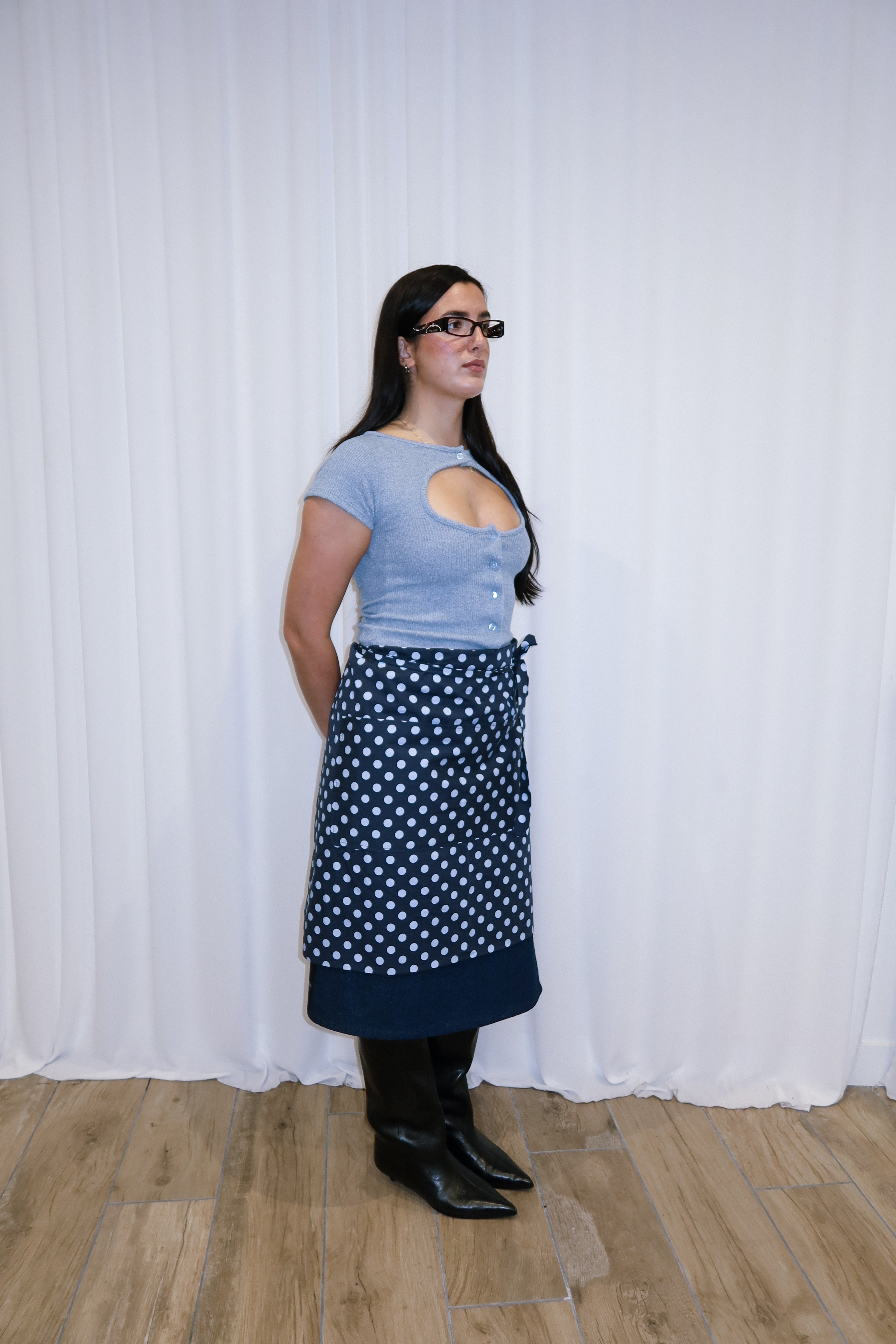 Woman wearing a navy polka dot apron against a white curtain background.