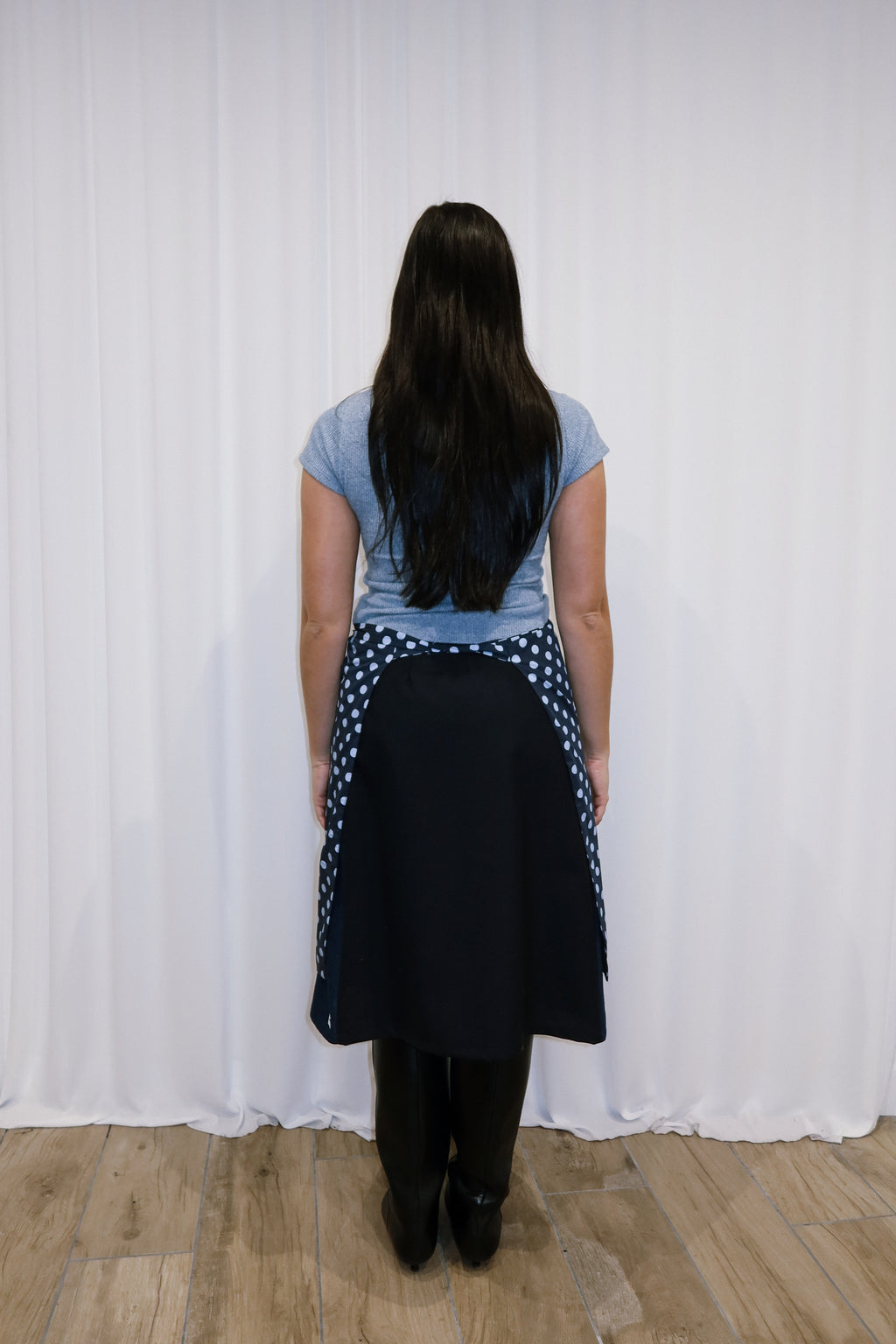 Woman wearing a navy polka dot apron against a white curtain background.